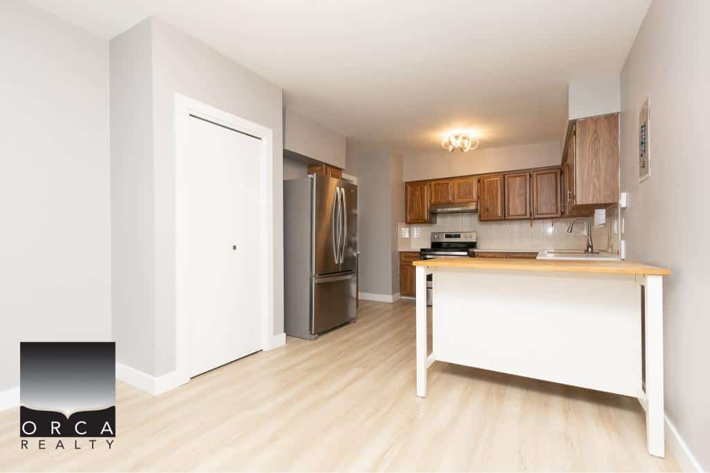 Bright modern kitchen with stainless steel appliances, wooden cabinets, and a breakfast bar in a contemporary condo. Perfect for cozy living and cooking in a prime location in the Vancouver area.