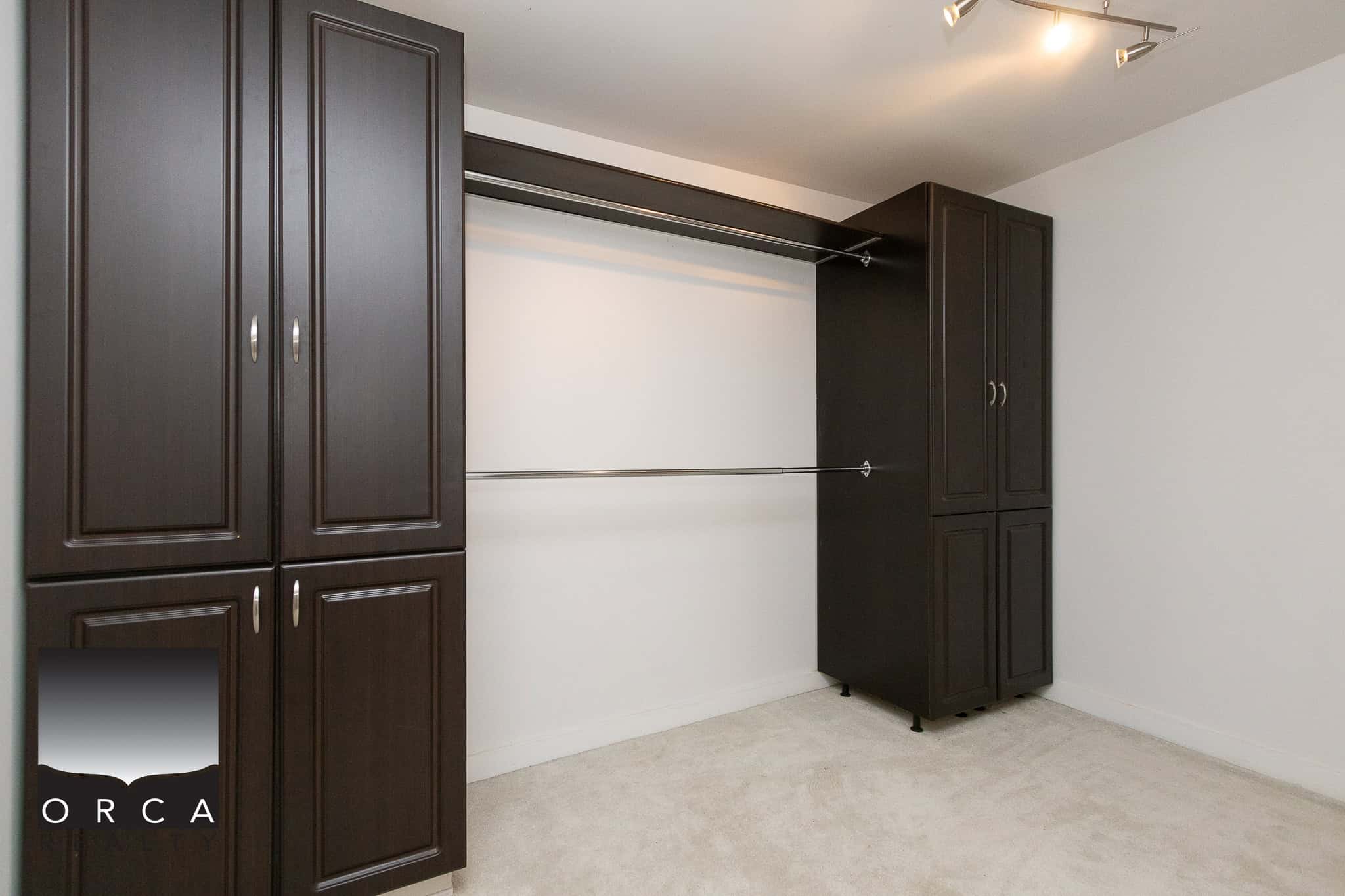 Spacious walk-in closet with dark wood storage cabinets and hanging rods, ideal for organizing clothing and accessories in a modern home. Perfect for maximizing storage space.