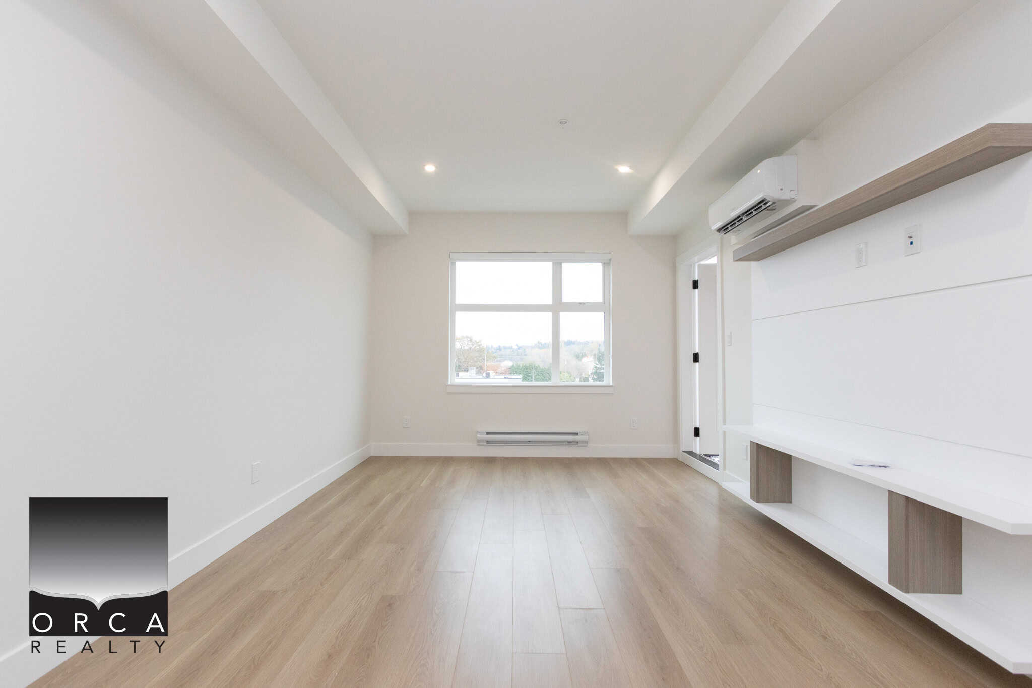 Bright, modern living room with white walls, large window, light wood flooring, and built-in media wall, showcasing contemporary interior design by Orca Realty Inc. for Vancouver real estate.