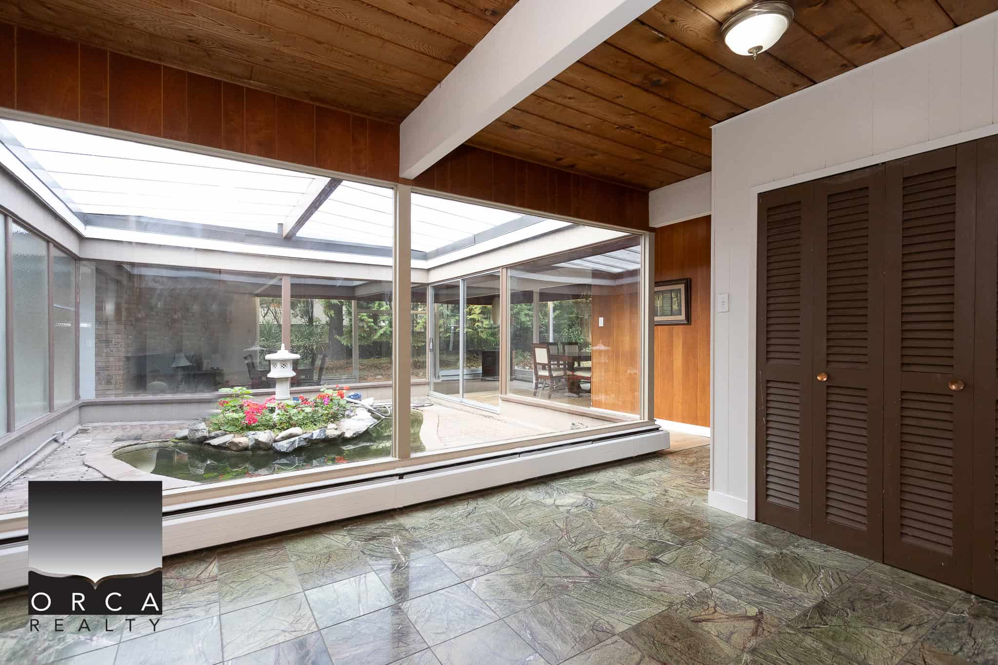Bright sunroom with large glass sliding doors overlooking outdoor pond and garden, featuring wooden ceiling and stone tile flooring, perfect for relaxing and enjoying nature in your Vancouver home.
