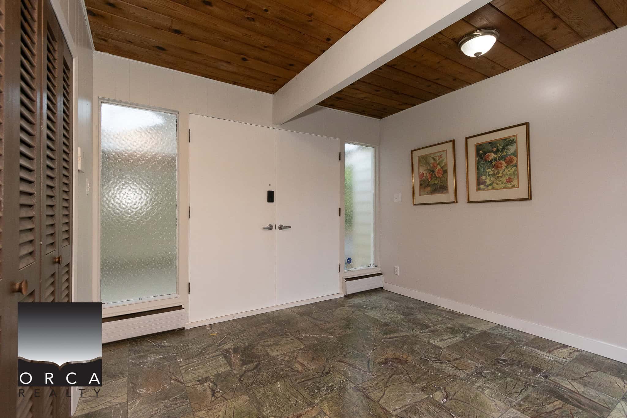 Cozy entryway with textured glass door, wooden ceiling, and vintage floral artwork, offering a welcoming atmosphere for Vancouver Island real estate.