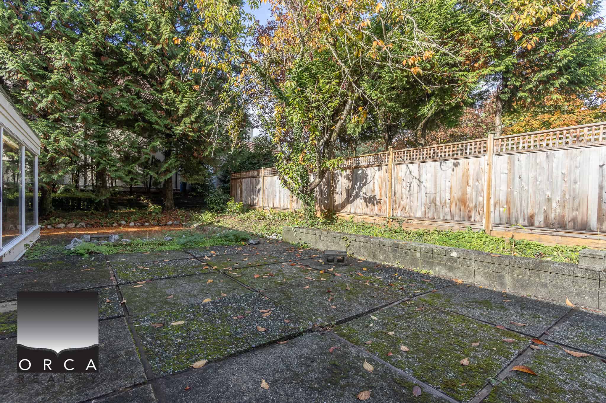 Spacious backyard with mature trees, fenced yard, and moss-covered concrete patio, perfect for outdoor living and landscaping in Nanaimo, BC.