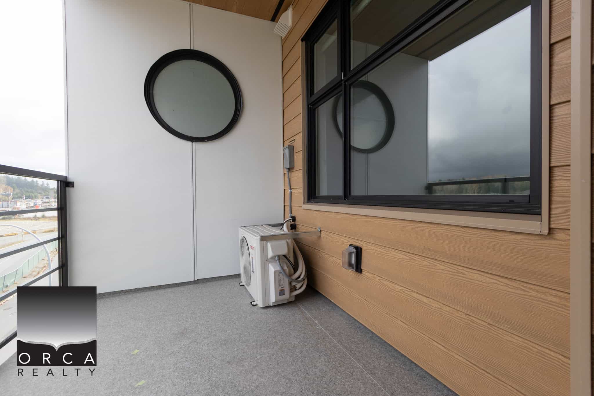Modern balcony with window, circular mirror, and outdoor air conditioning unit in a contemporary Vancouver-area home.