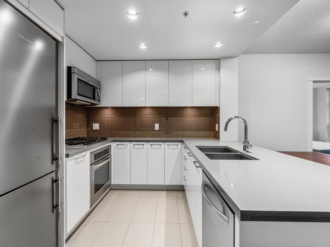 Modern kitchen with white cabinets, stainless steel appliances, and a brown tile backsplash, perfect for stylish home living in BC.