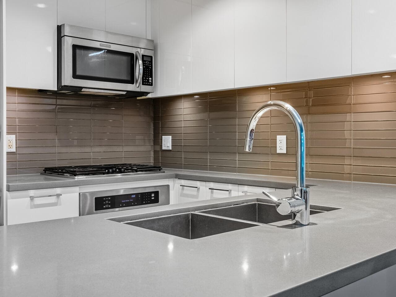 Modern kitchen with stainless steel microwave, gas stove, sleek white cabinetry, and beige tile backsplash, perfect for contemporary homes in Vancouver, BC.