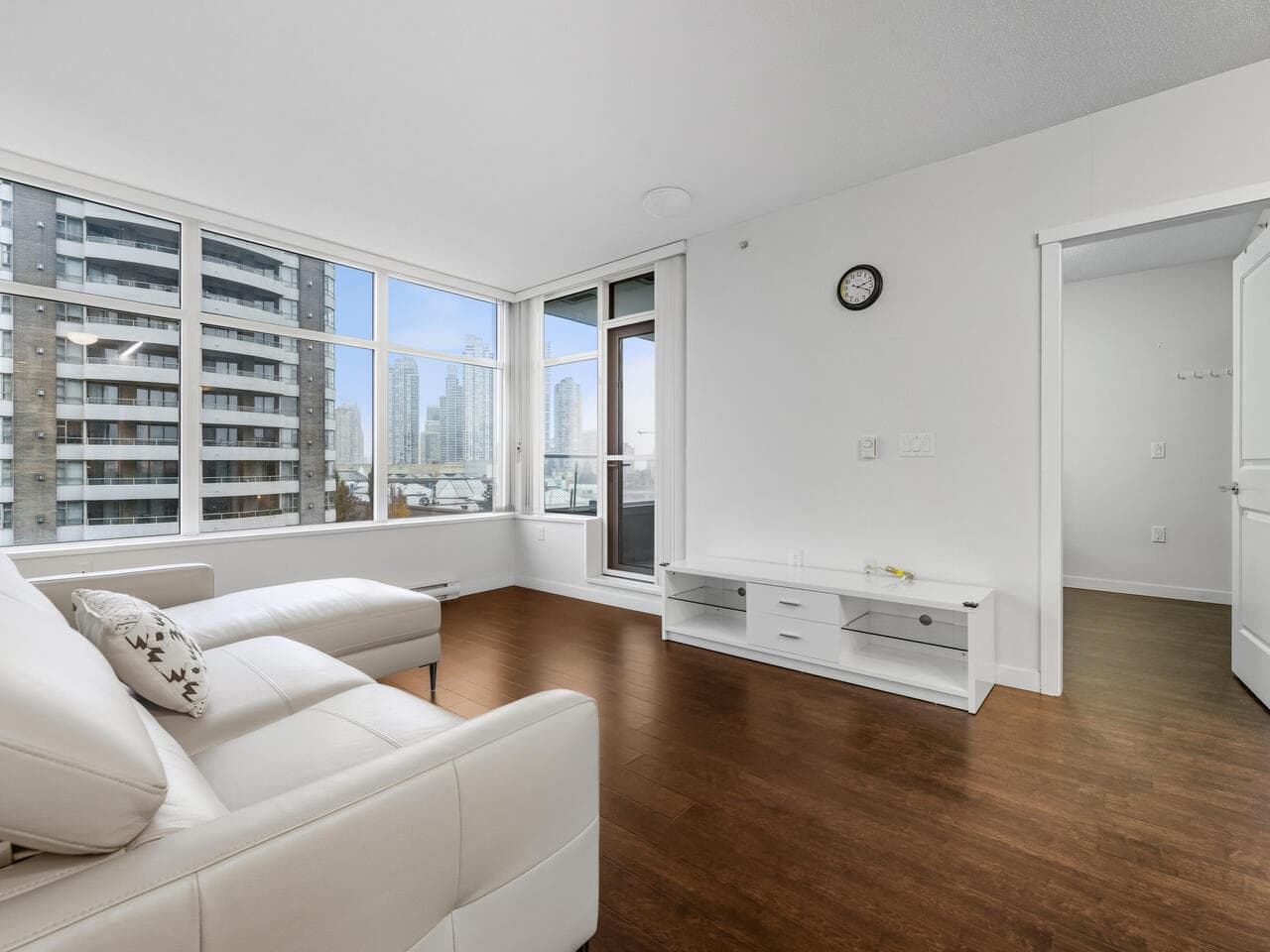 Bright living room with large windows, modern condo in downtown Vancouver featuring hardwood floors, white walls, and city skyline views. Ideal for urban living with convenient access to amenities.