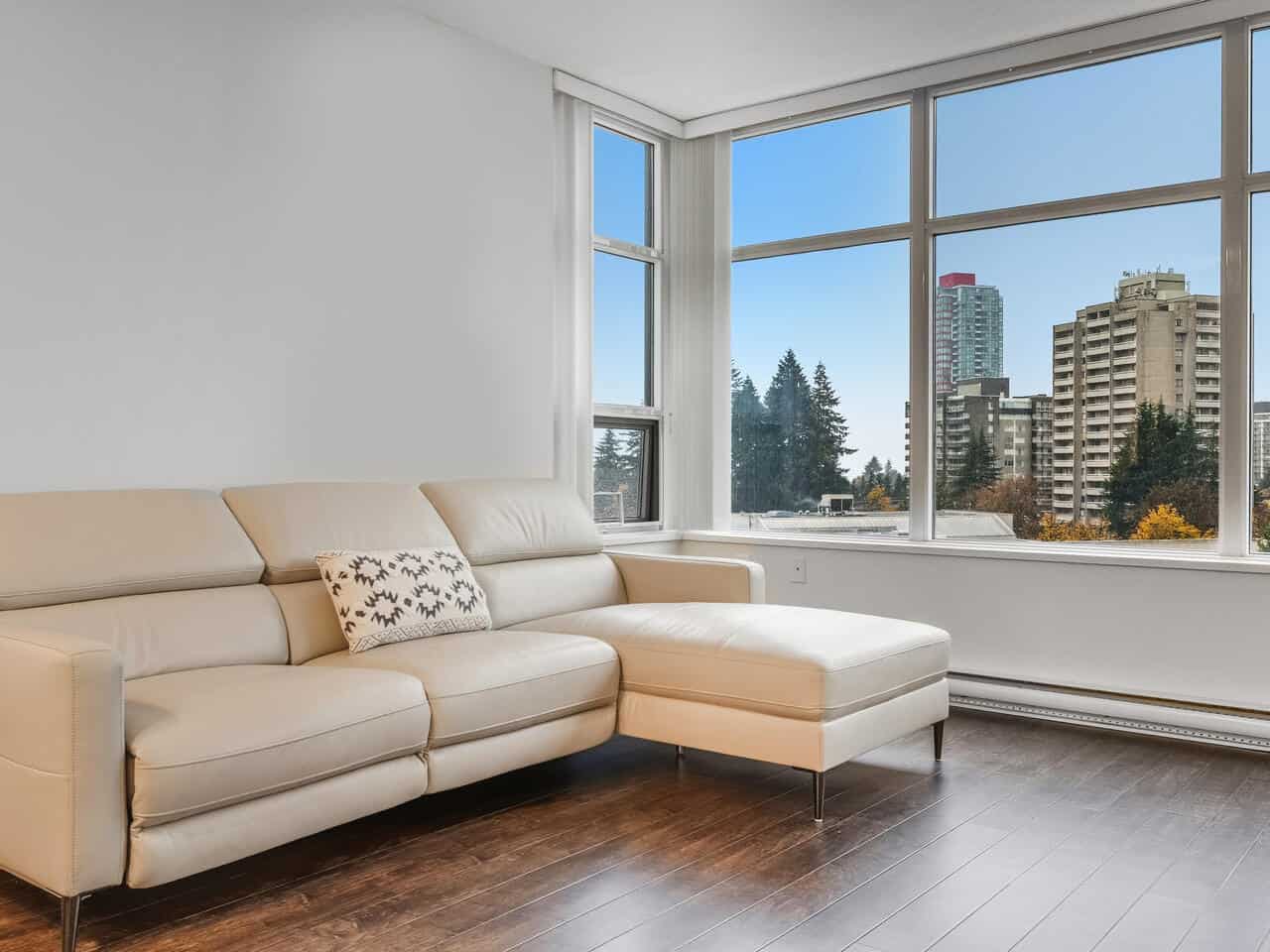 Modern high-rise apartment with large windows offering city views, bright and spacious living room with elegant cream sectional sofa, ideal for Vancouver real estate listings.