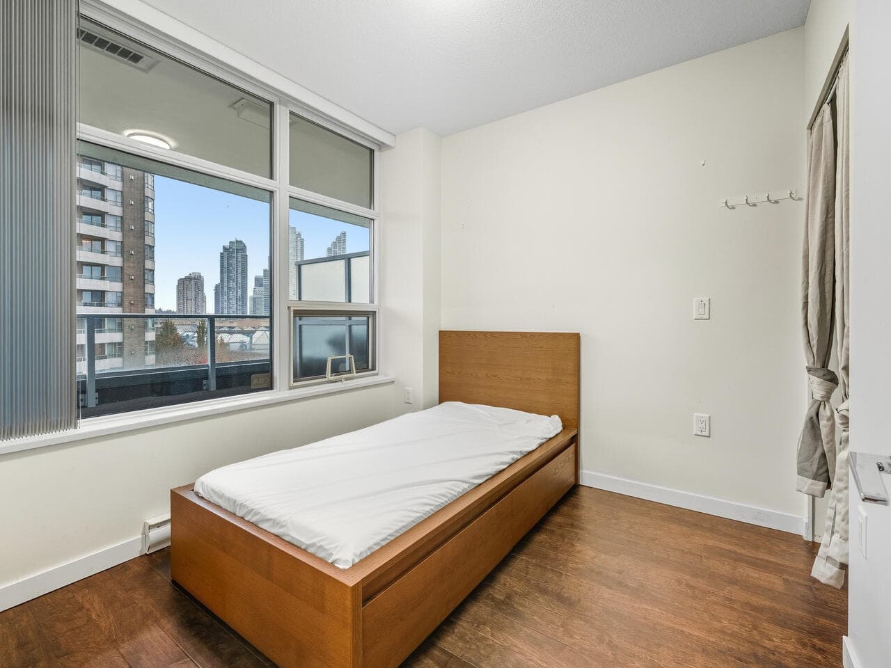 Bright furnished bedroom in Vancouver high-rise with city skyline views and large windows, ideal for rental or investment properties in downtown Vancouver real estate.