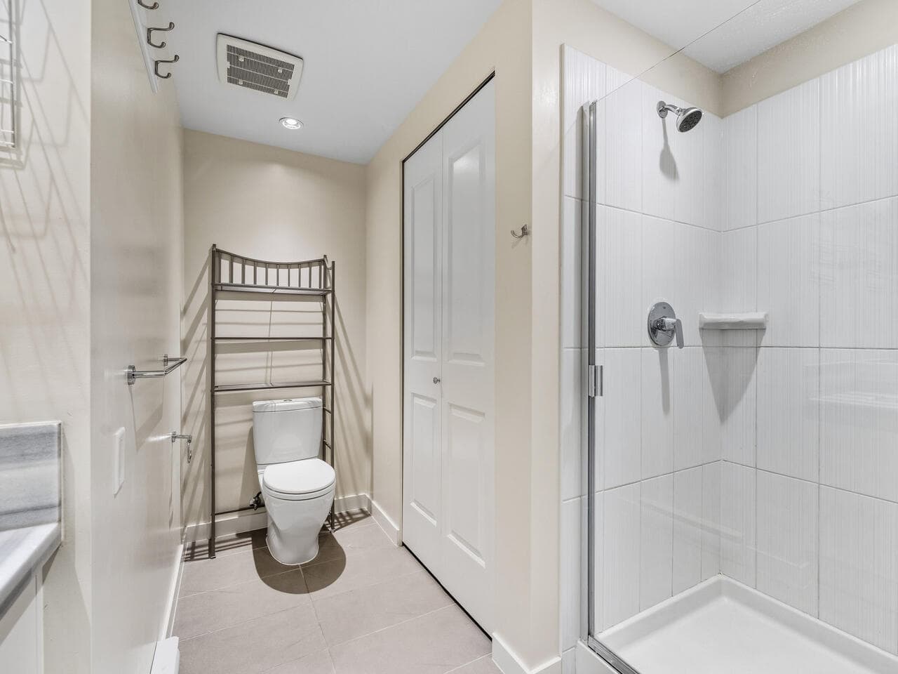 Modern minimalist bathroom with a clean design, featuring a white toilet, compact shelving unit, and a spacious walk-in shower with white tiled walls, perfect for Vancouver Island living.