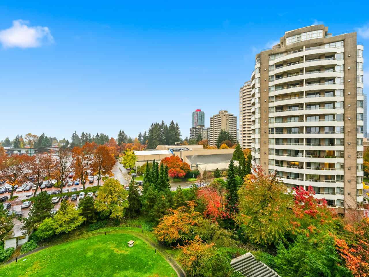 Vibrant cityscape view from Orca Realty Inc. showcasing modern high-rise apartments, lush green park with fall foliage, and urban skyline in the background on a clear autumn day in Vancouver, BC.