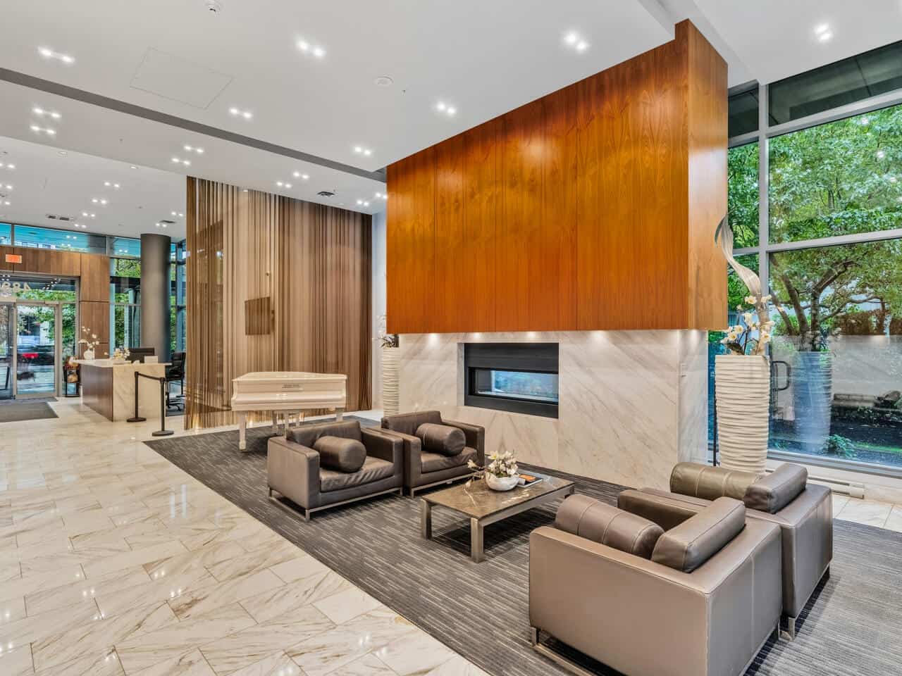 Bright, modern lobby with contemporary furniture, marble flooring, and large windows showcasing greenery, featuring a sleek fireplace and high-end interior design, representing Orca Realty Inc.'s professional real estate services.
