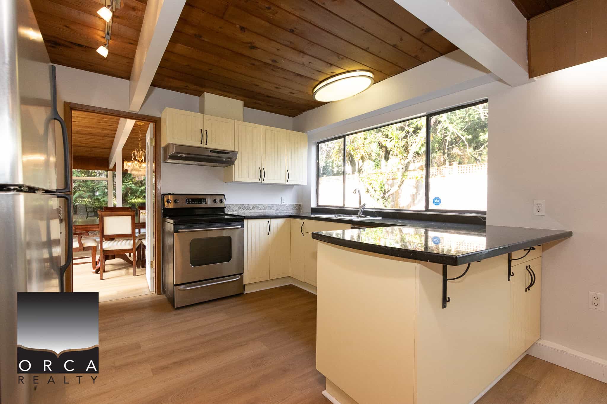 Bright kitchen with large window, stainless steel appliances, cream cabinetry, and wood accents, perfect for homebuyers seeking modern comfort in a scenic setting.