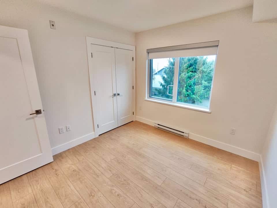 Bright and clean empty bedroom with large window, carpeted closet, and light wood flooring, ideal for Vancouver Island real estate buyers seeking modern homes in the Orca Realty area.
