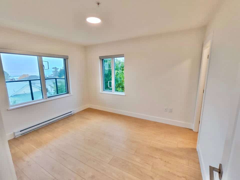 Bright empty living room with large windows and hardwood flooring, ideal for Vancouver Island real estate buyers seeking modern, spacious homes in a peaceful neighborhood.