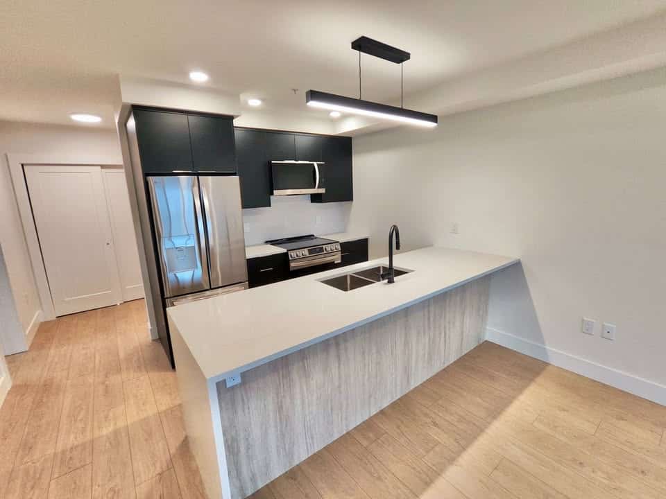 Modern kitchen with black cabinets, stainless steel appliances, and a spacious white island countertop, ideal for Vancouver real estate listings and showcasing contemporary condo features.