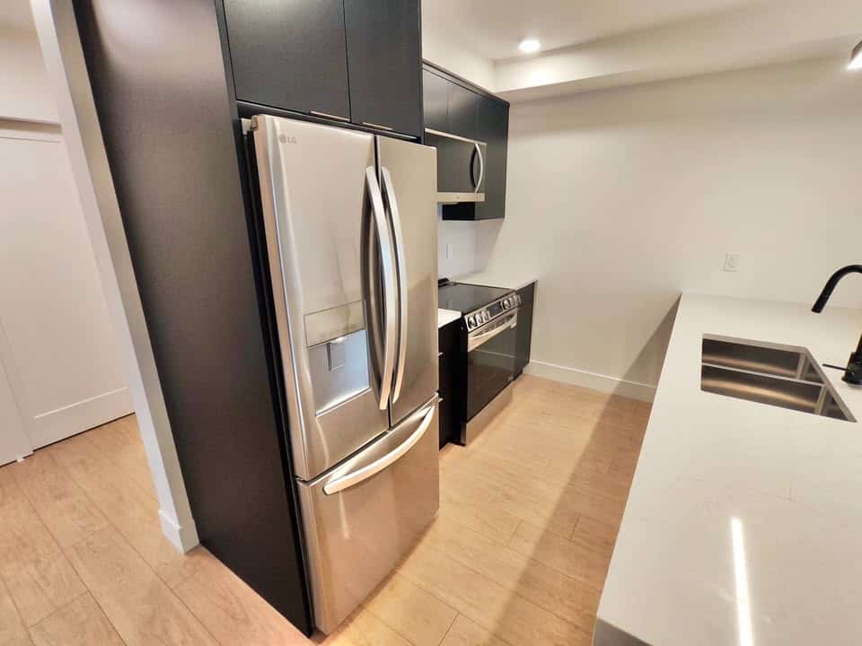 Stainless steel refrigerator in modern kitchen with black cabinetry and white countertops, showcasing contemporary home appliances.