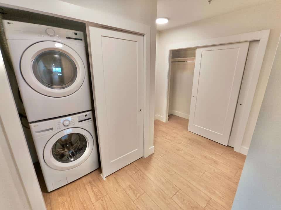 Stacked washer and dryer in a closet with white doors and hardwood flooring, part of a modern residential laundry area.