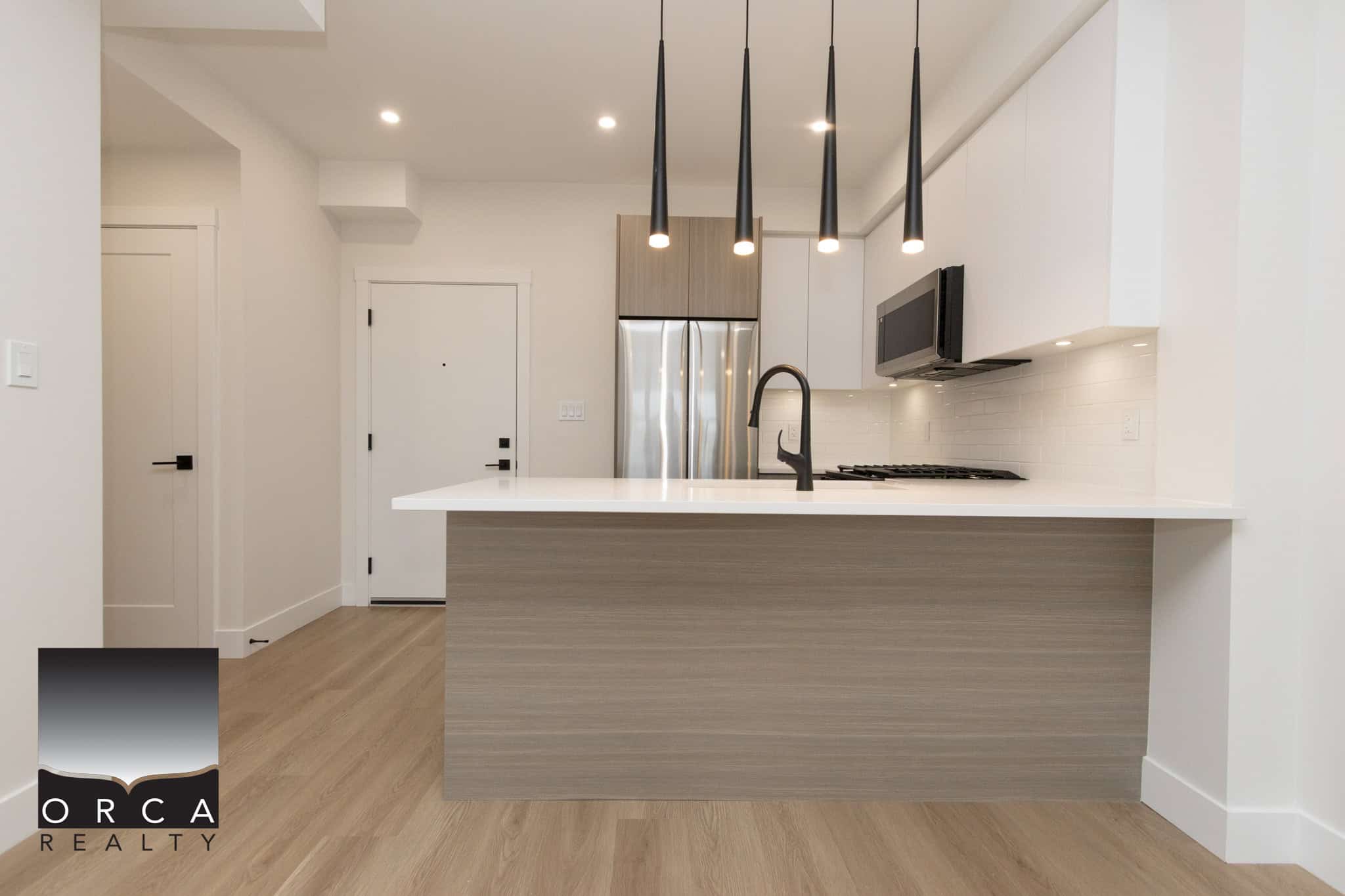 Contemporary modern kitchen with minimalist design, white cabinets, black pendant lighting, stainless steel appliances, and light wood flooring, perfect for Edmonton homebuyers.