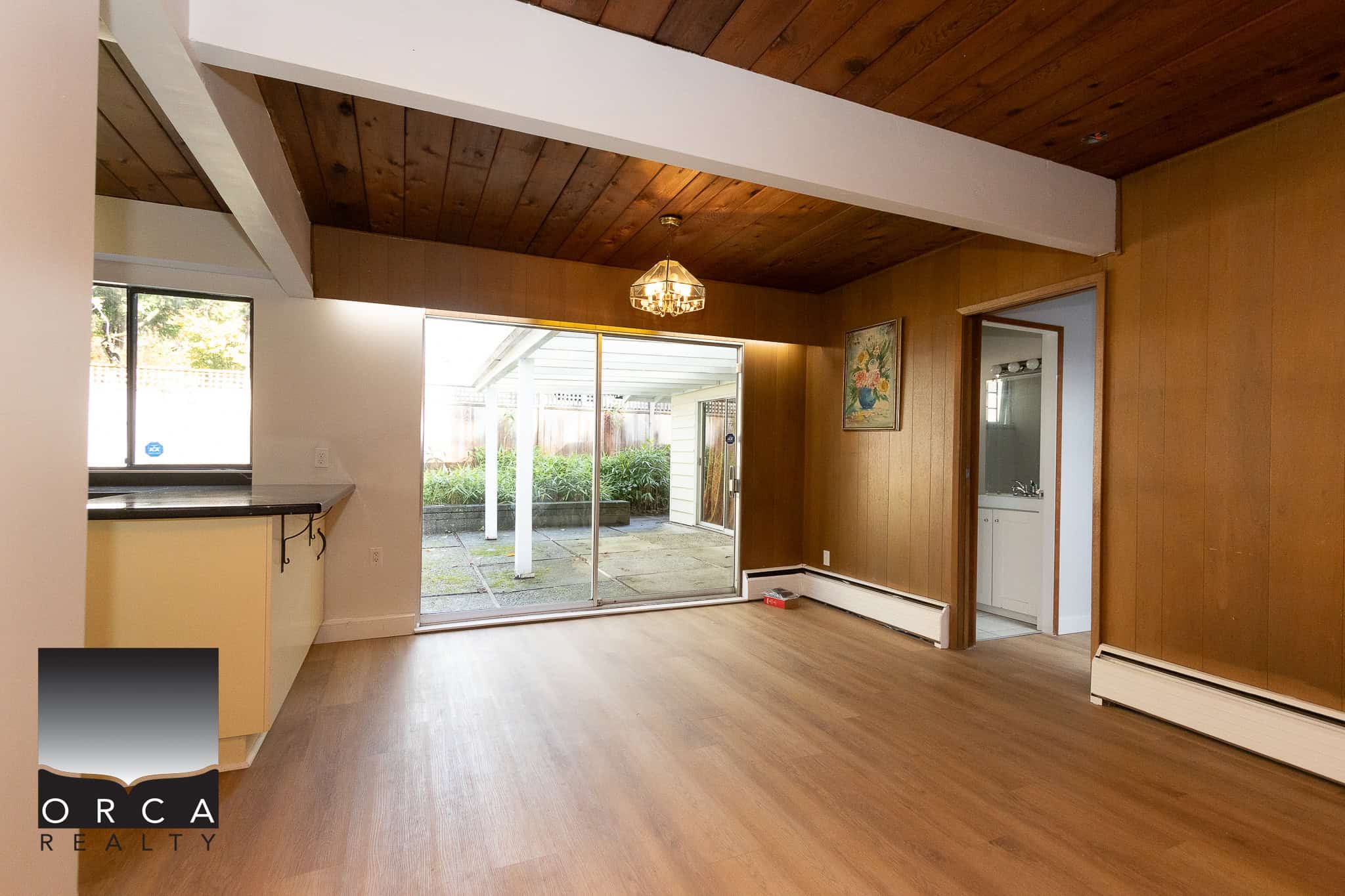 Bright interior living space with wood-paneled walls and sliding glass doors leading to a backyard patio, showcasing Orca Realty's expertise in Vancouver Island real estate.