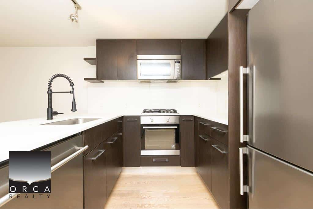 Modern dark wood kitchen with stainless steel appliances including microwave, oven, and refrigerator, white countertop and black faucet, ideal for Toronto area real estate listings.