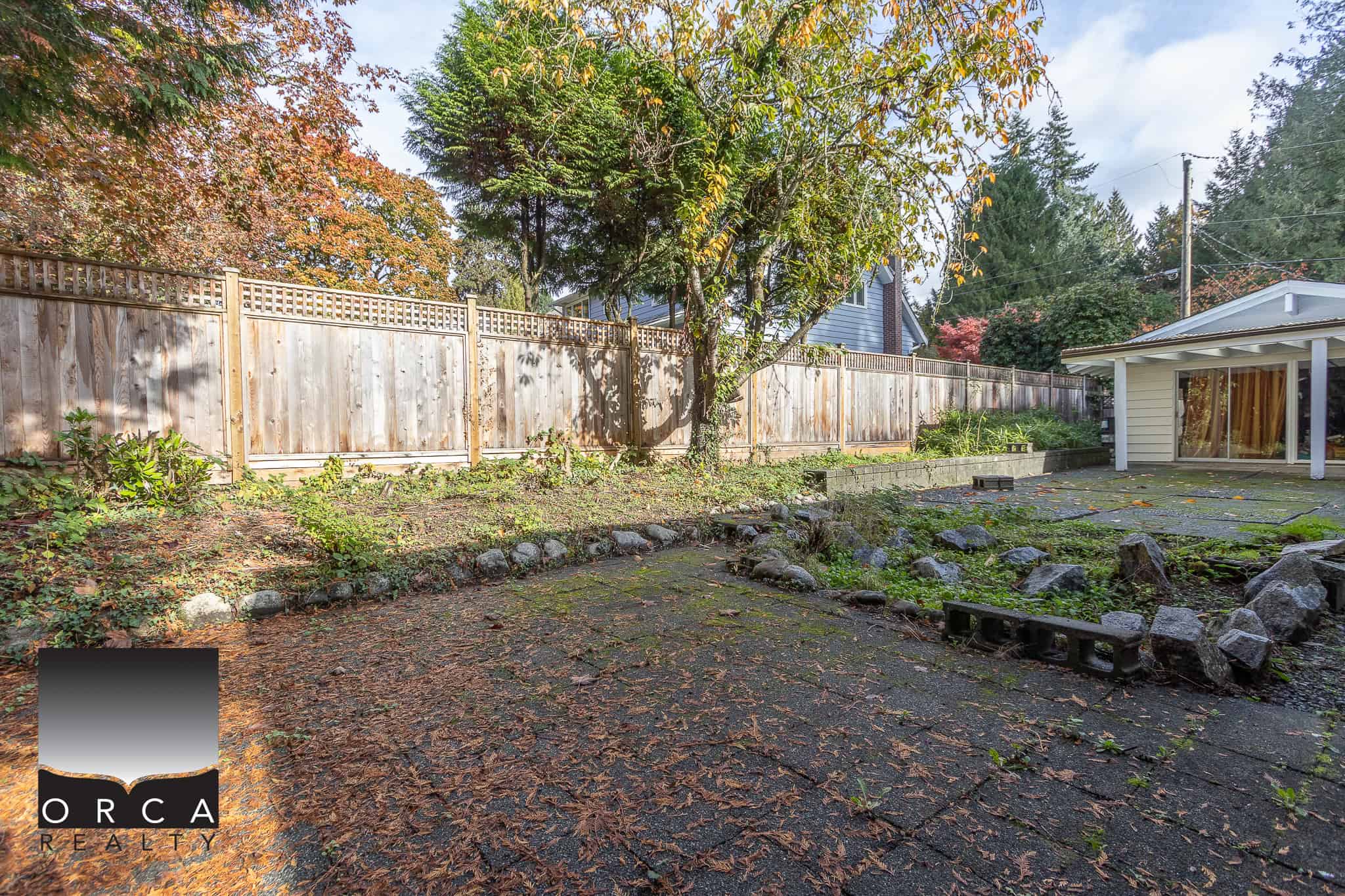 Lush backyard with mature trees, wooden fence, and outdoor patio space, perfect for Vancouver Island real estate, residential property, or investment opportunities.