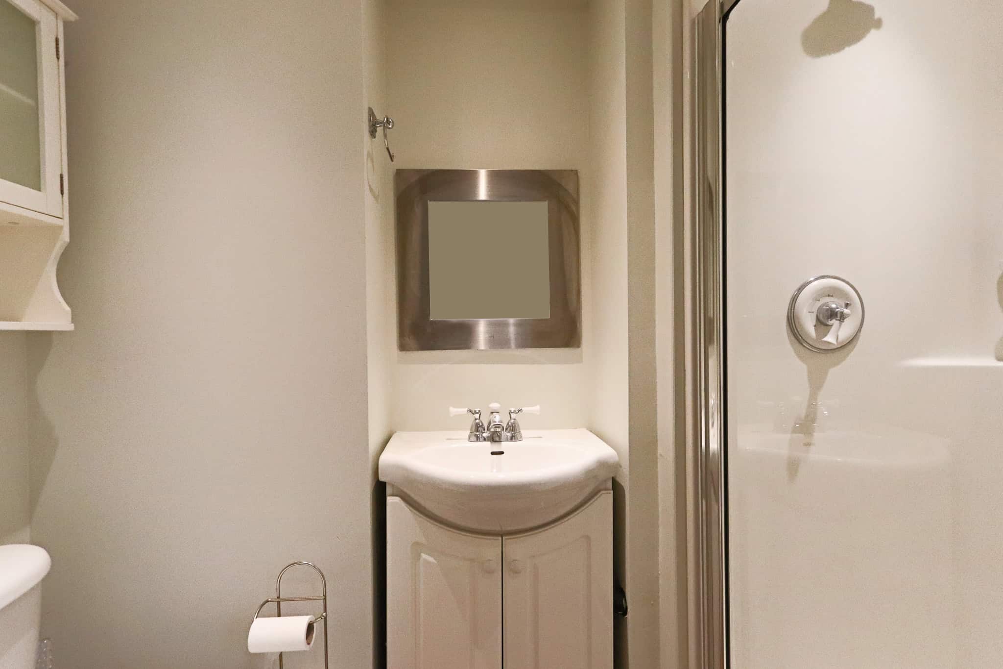 Clean small bathroom with white vanity, wall mirror, and enclosed shower, showcasing modern fixtures and neutral decor, ideal for cozy home or rental property.