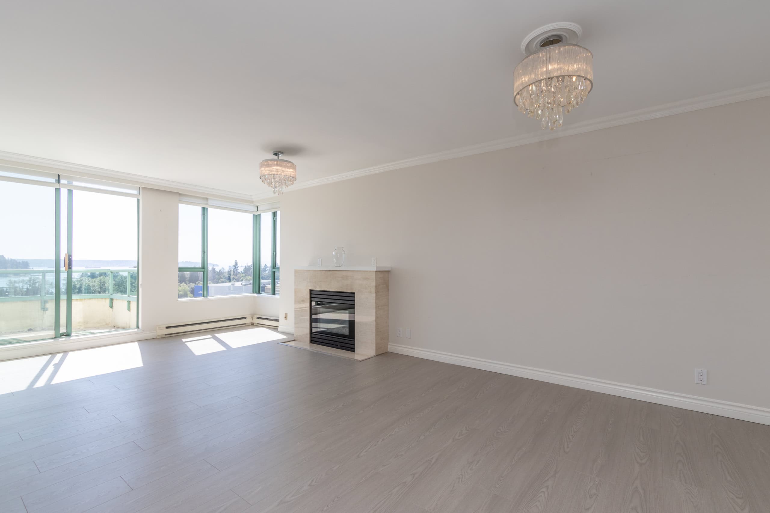 Spacious living room with panoramic windows, modern fireplace, and elegant chandeliers in a Vancouver-area apartment by Orca Realty Inc.