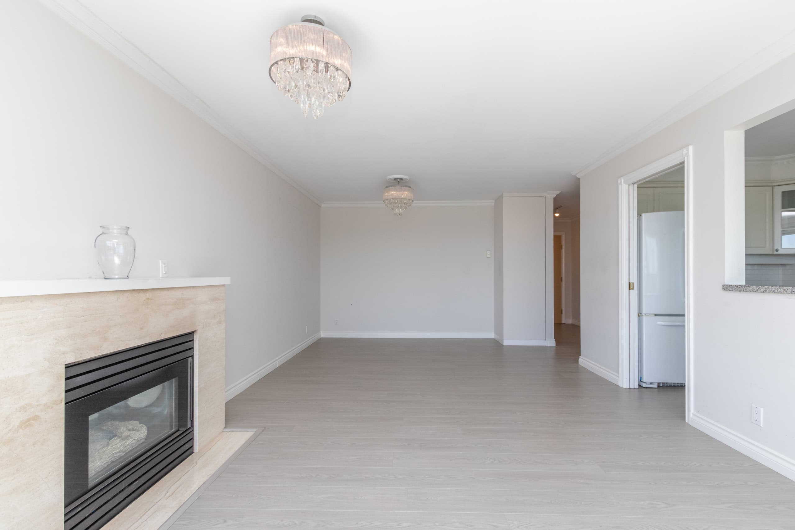 Spacious living room with modern fireplace and elegant chandelier, featuring neutral-colored walls and flooring, ideal for Vancouver real estate buyers seeking stylish homes.