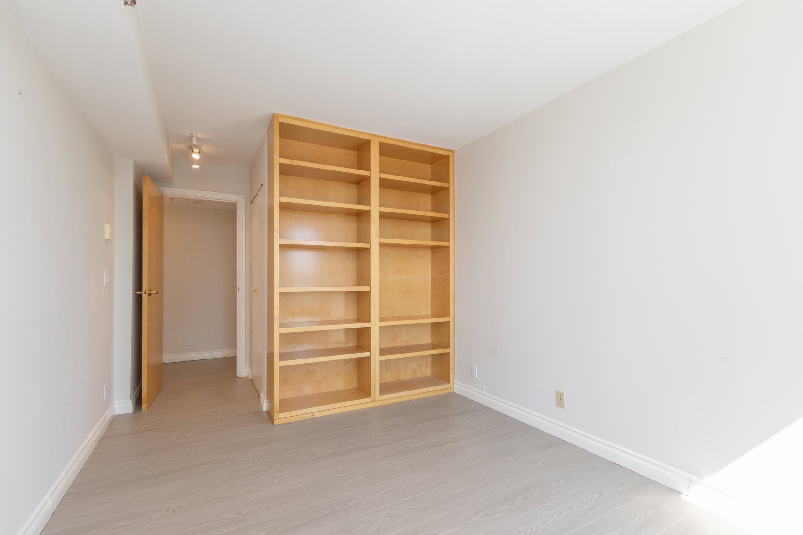 Spacious empty room with built-in wooden shelves, bright white walls, and light grey flooring, ideal for Vancouver real estate listings.