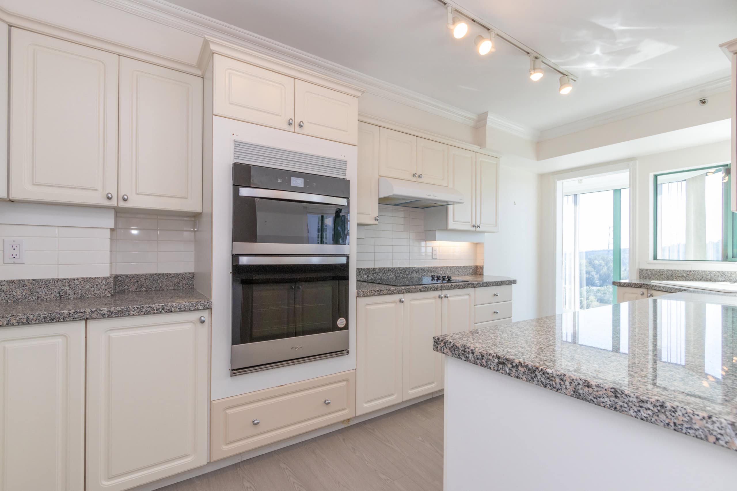 Bright modern kitchen with white cabinets, granite countertops, stainless steel oven, and large windows overlooking scenic views, ideal for real estate listings and home tours in Vancouver.
