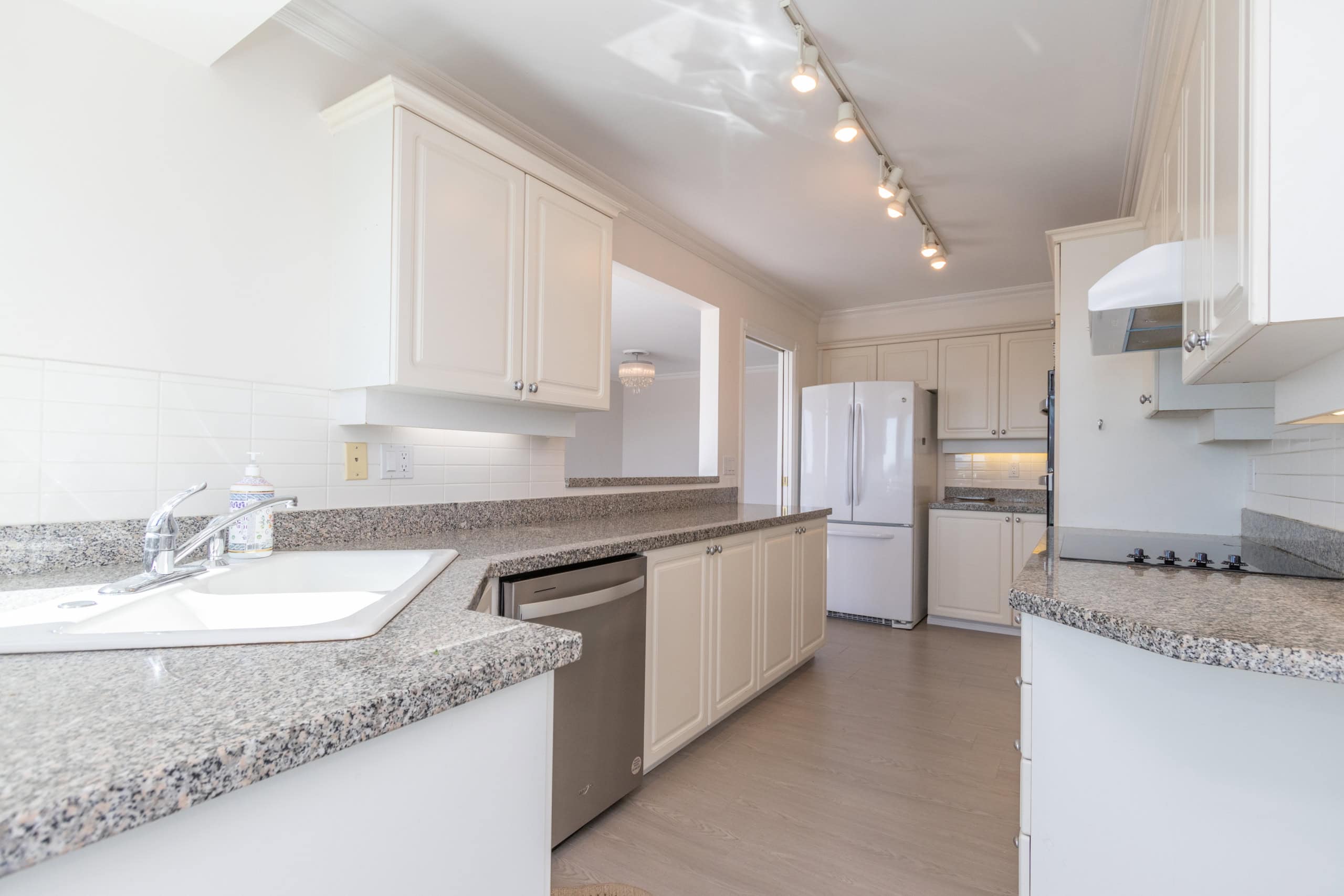 Modern white kitchen with granite countertops, stainless steel appliances, and ample cabinetry, ideal for homebuyers seeking a stylish and functional kitchen space.