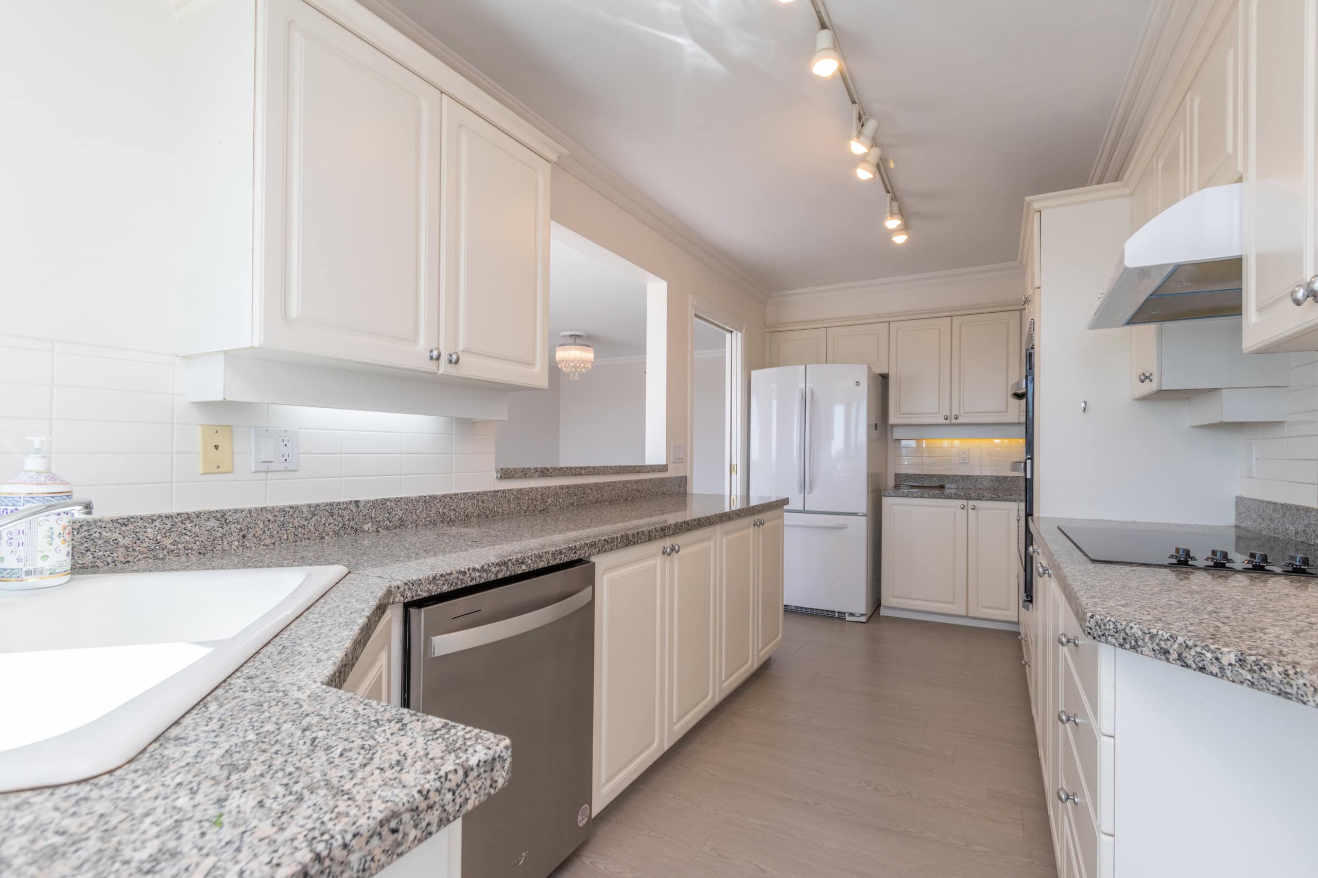 Spacious white kitchen with granite countertops and modern appliances, ideal for homebuyers in Vancouver. Kitchen features ample cabinet storage, a built-in dishwasher, and updated fixtures, perfect for family living or entertaining.