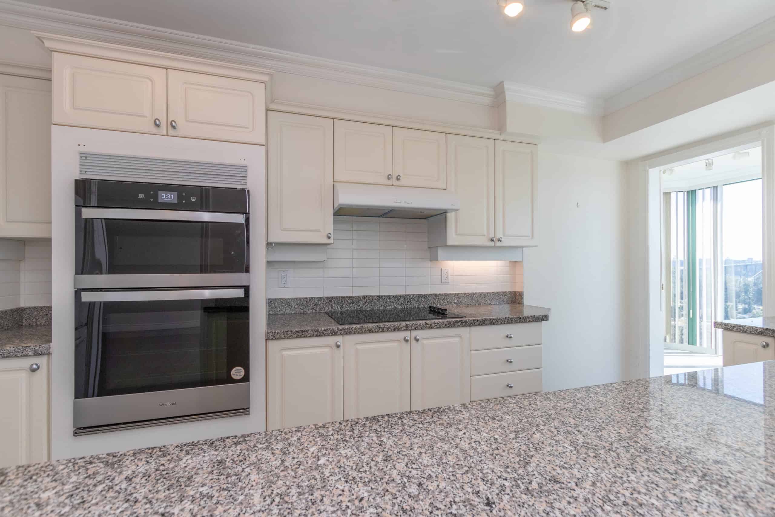 Spacious white kitchen with granite countertops, built-in oven, and ample cabinet storage showcasing Orca Realty Inc.'s professional real estate services.