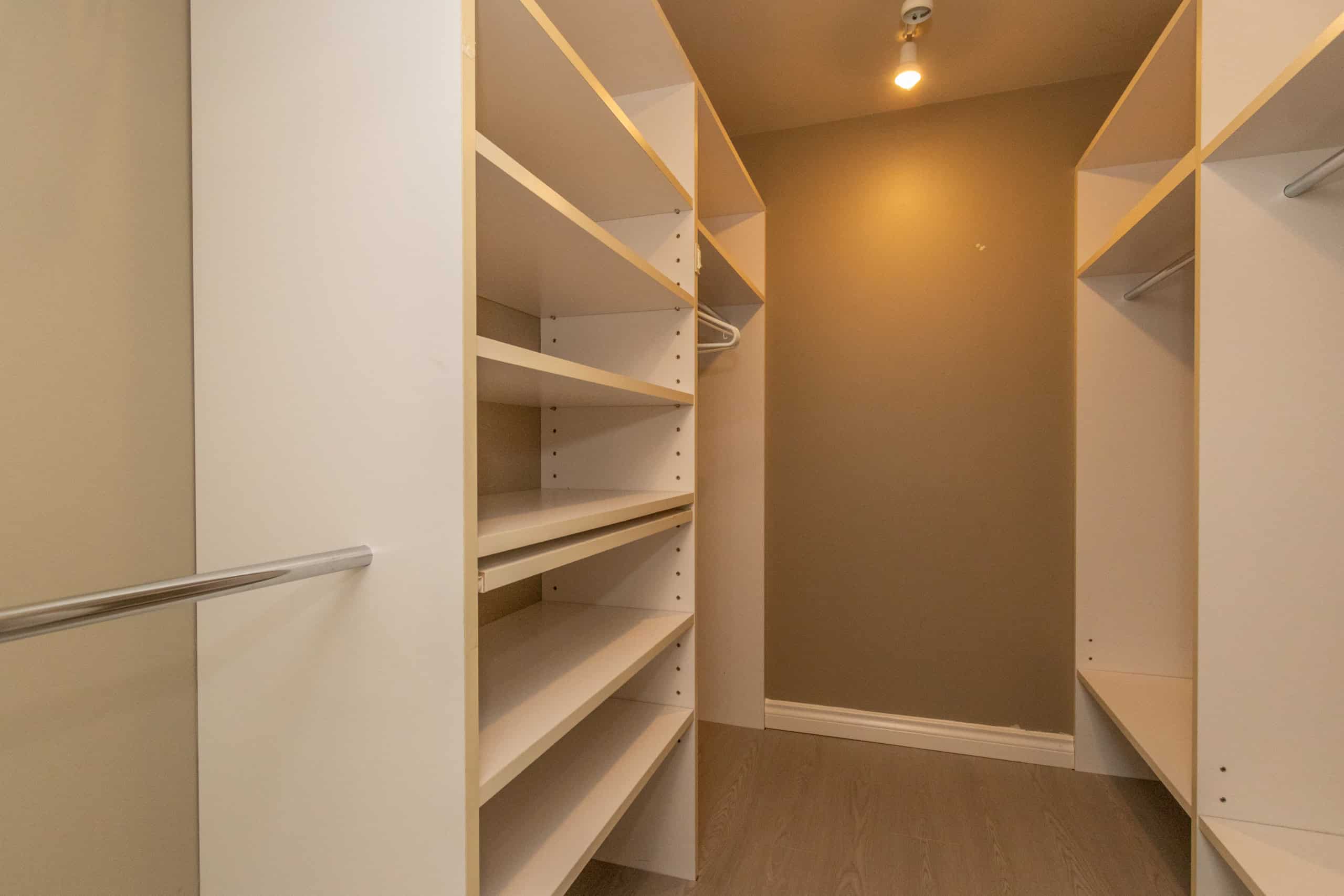 Spacious walk-in closet with custom shelving and hanging rods, ideal for organizing a Vancouver home. Modern interior design featuring ample storage solutions and neutral tones.