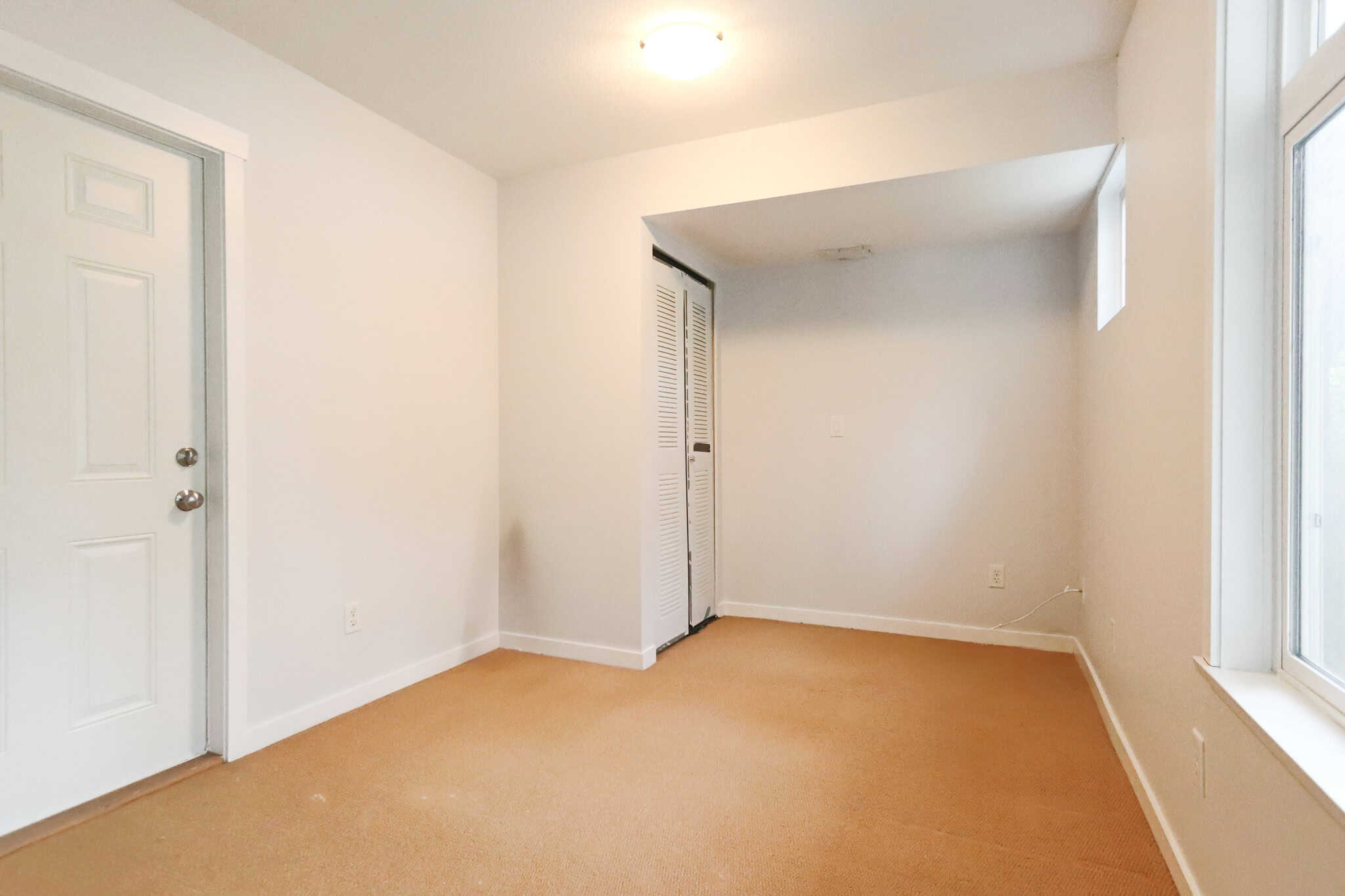 Bright empty room with beige carpet, white walls, large window, and closet space, ideal for Vancouver real estate listings.