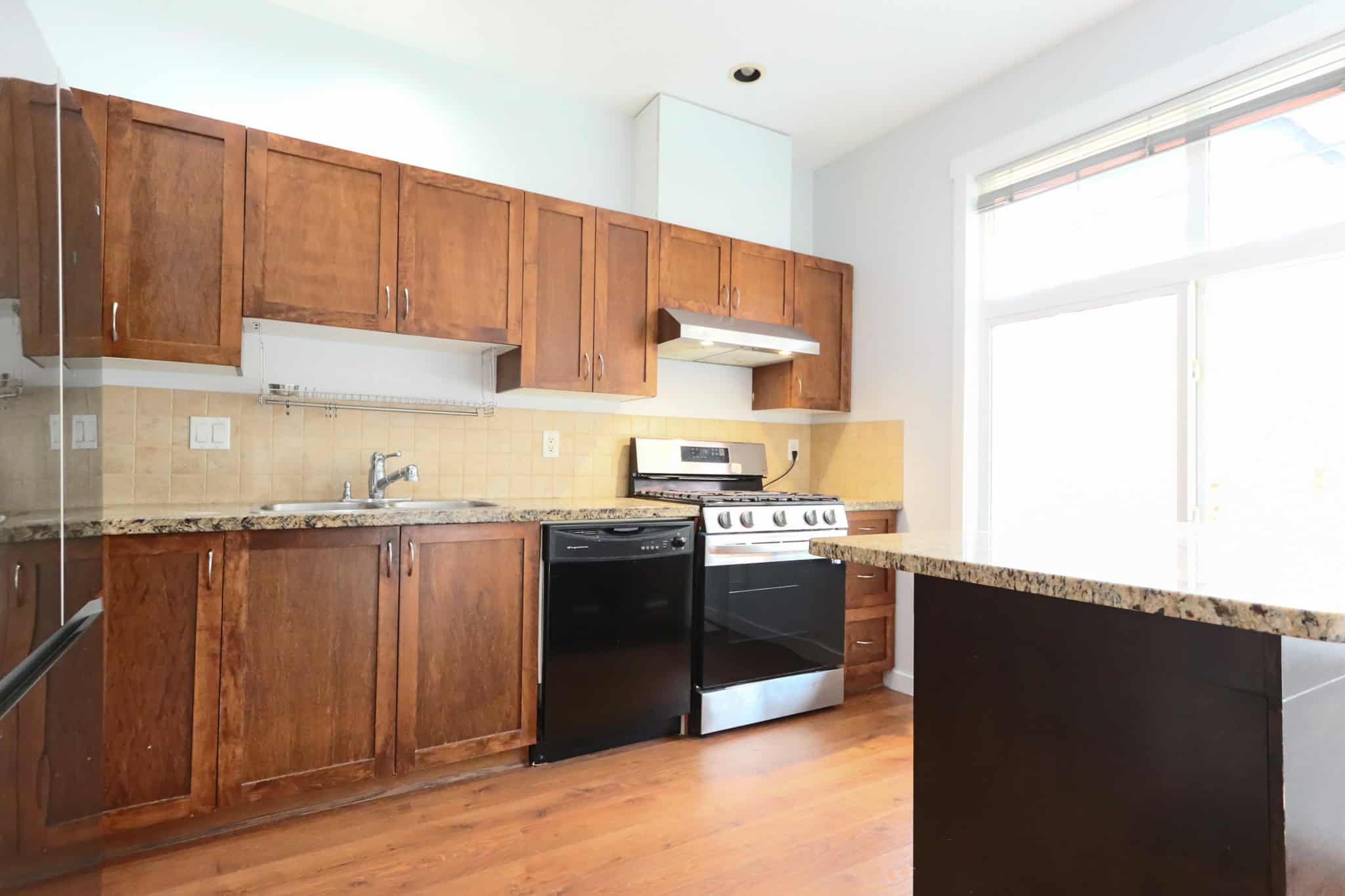 Spacious kitchen with wooden cabinets, granite countertops, stainless steel stove, and large window allowing natural light, ideal for Vancouver Island real estate listings.