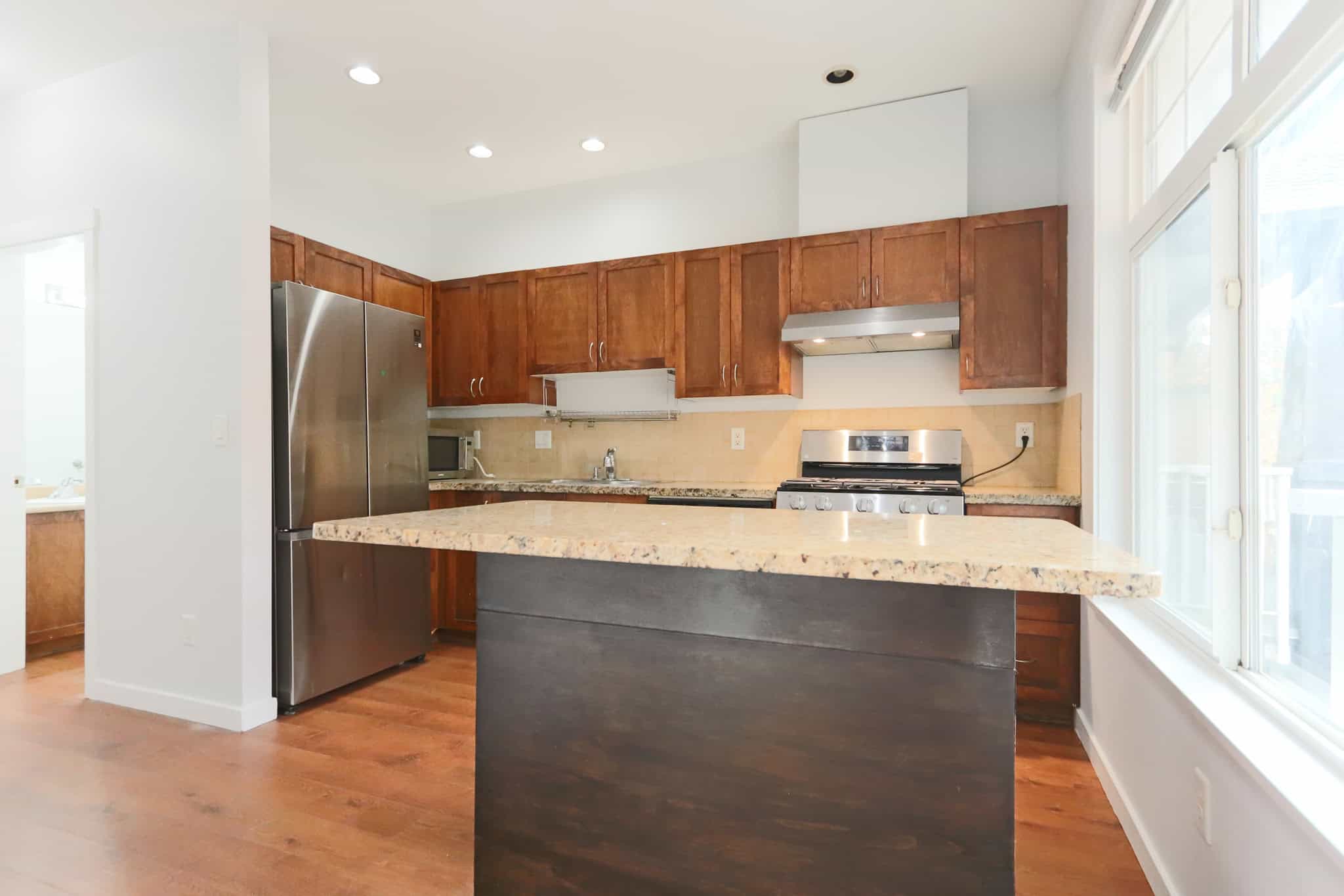 Modern kitchen with wooden cabinets, granite countertops, stainless steel appliances, spacious island, and large windows providing natural light.