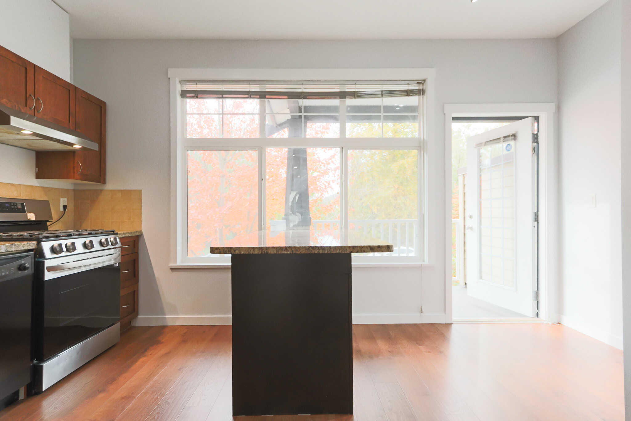 Bright modern kitchen with large window, stainless steel appliances, wooden cabinetry, and an island, ideal for homebuyers seeking stylish and functional Orca Realty Inc. properties in BC.