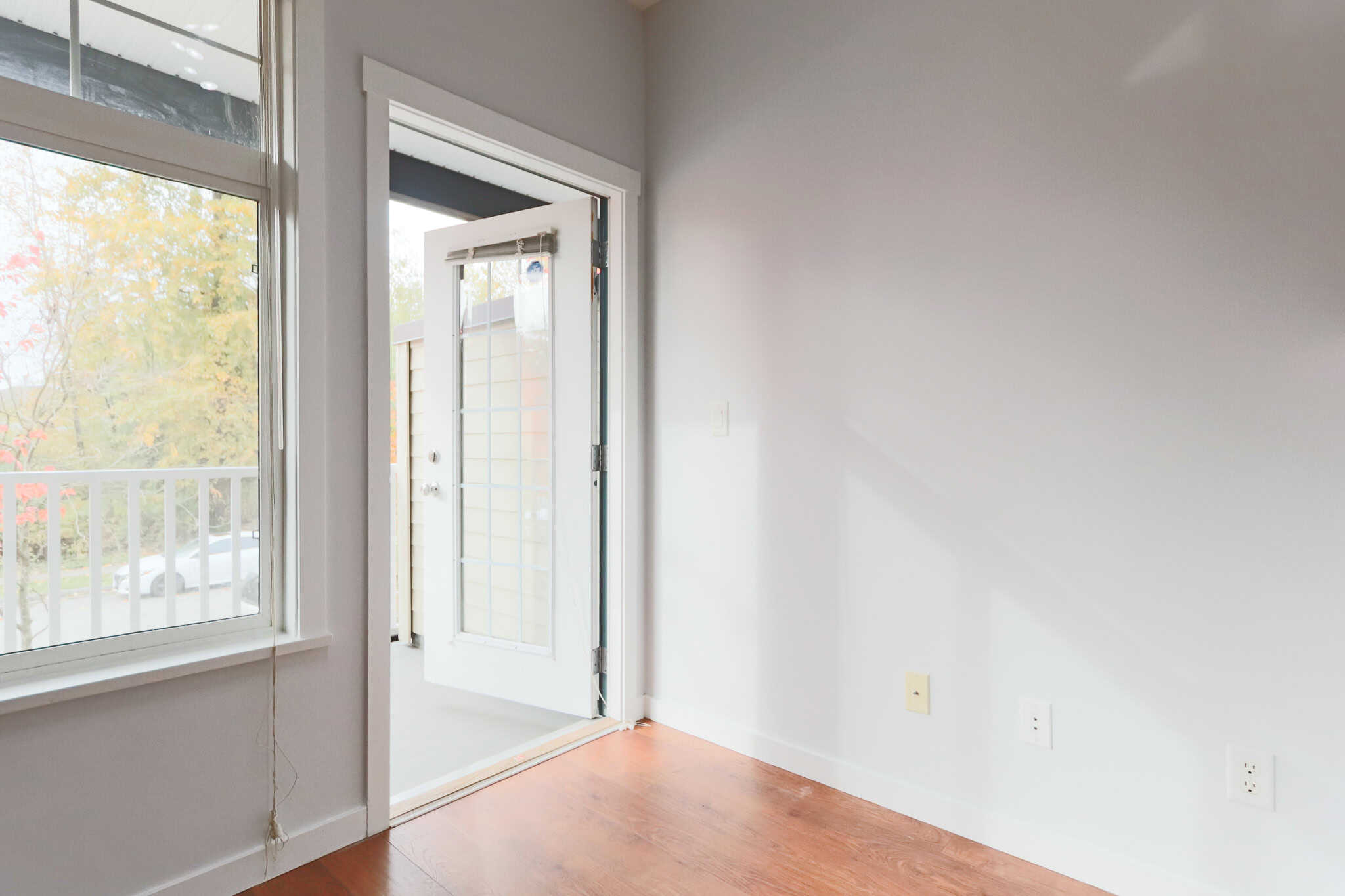 Bright interior of a modern home with white walls, hardwood flooring, large windows, and a glass door leading to a balcony, ideal for real estate listings.