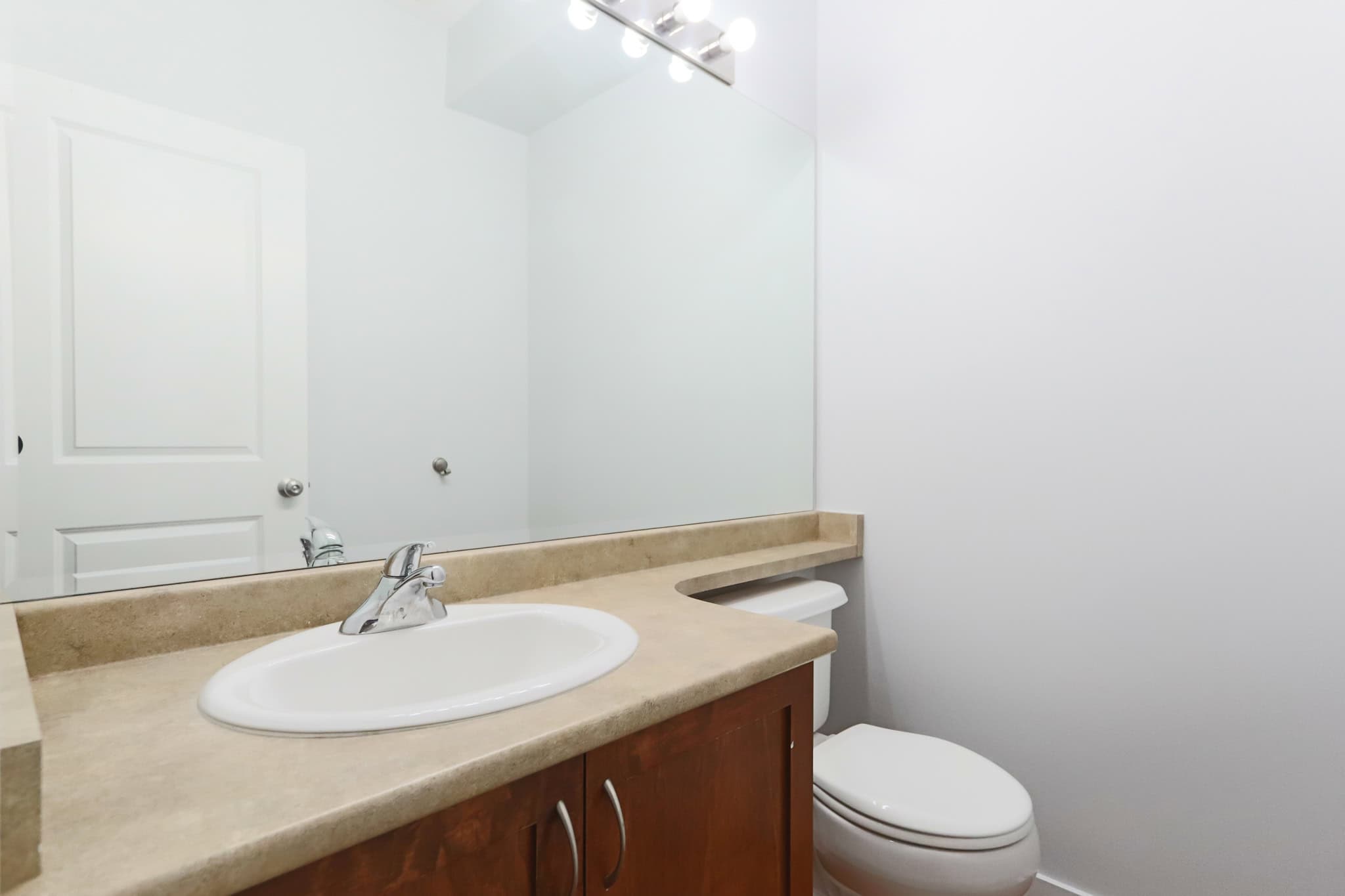 Clean modern bathroom interior with beige countertop, white sink, and wooden vanity, featuring ample mirror space and neutral wall colouring, ideal for Vancouver-area homes listed by Orca Realty Inc.