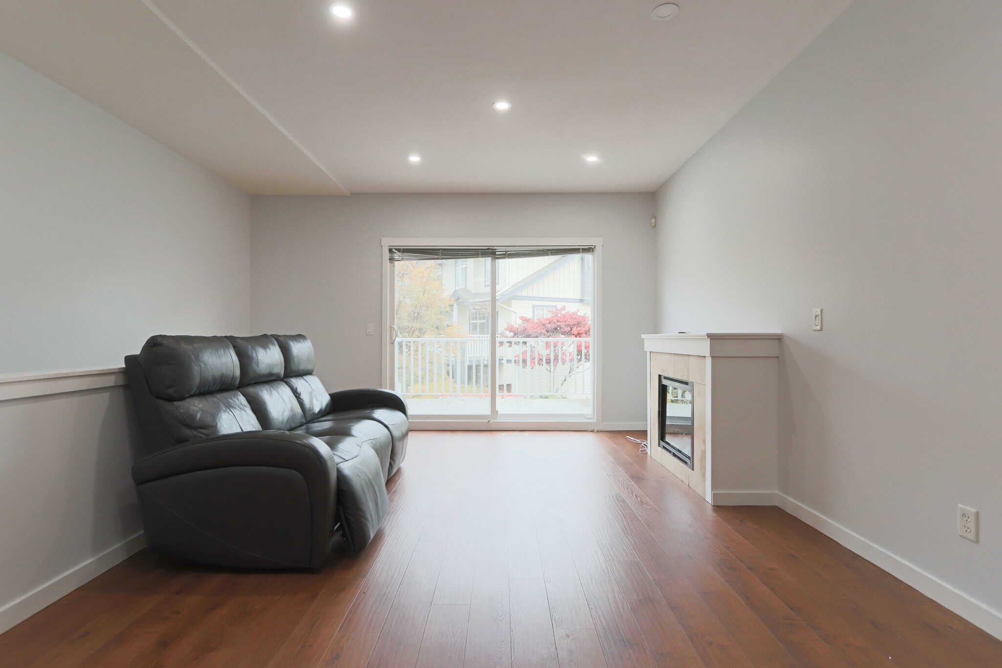 Bright living room with natural light, hardwood floors, modern fireplace, and sliding glass door leading to balcony, ideal for homebuyers and real estate listings in Vancouver.