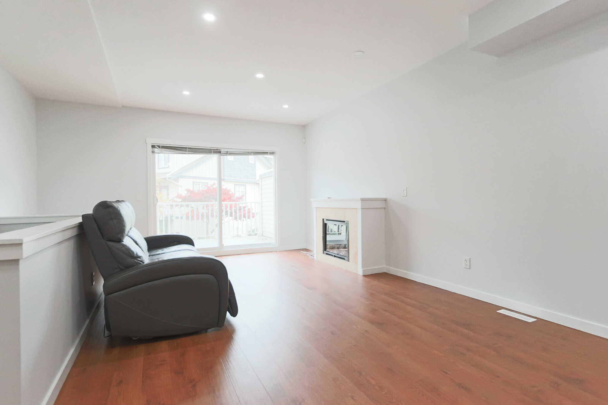 Contemporary living room with hardwood floors, white walls, and a fireplace, featuring natural light from sliding glass doors opening to a balcony, ideal for Vancouver area real estate.