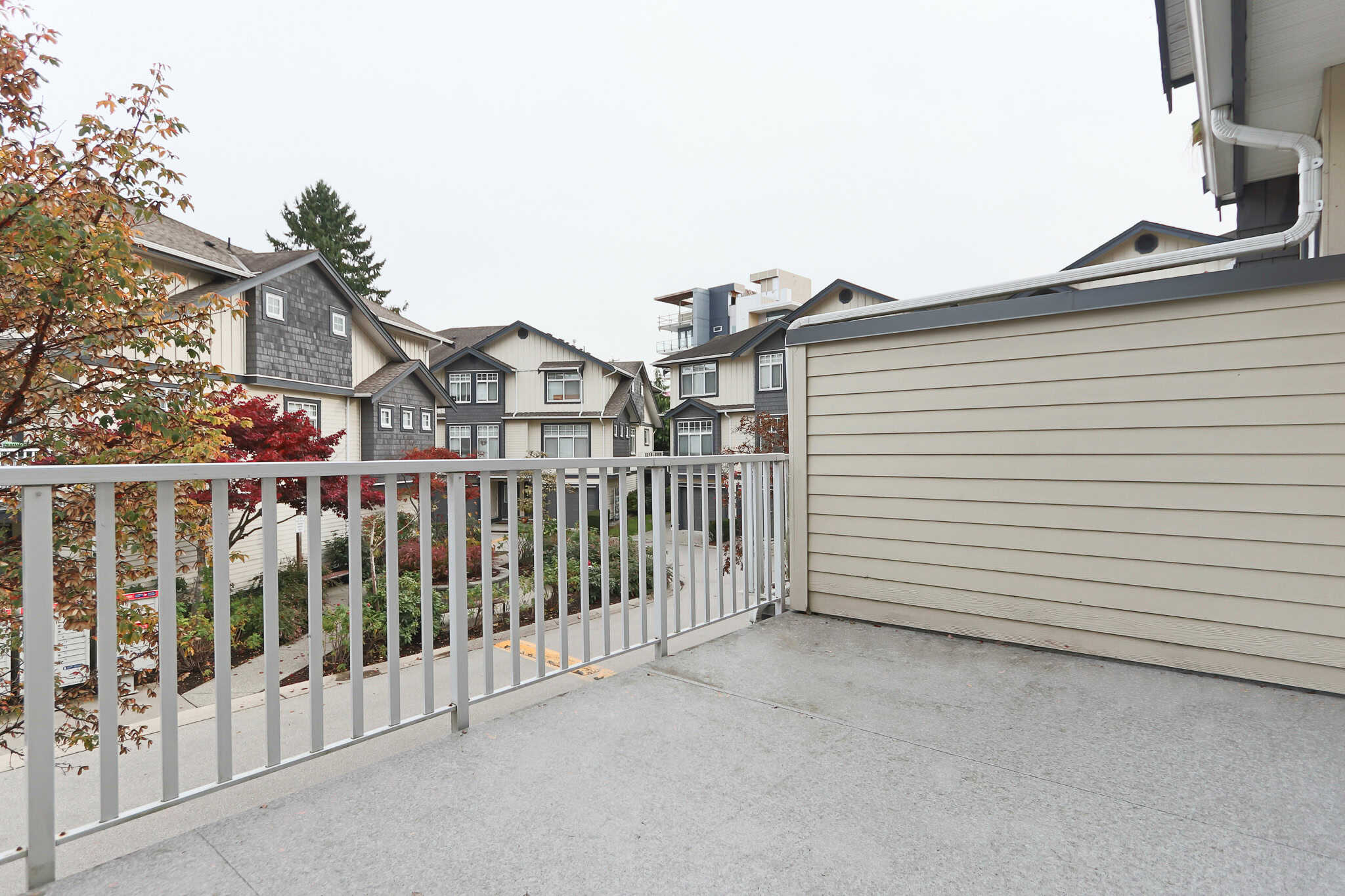 Bright balcony view of modern multi-family homes with decorative trees in a vibrant neighbourhood, showcasing residential outdoor space and urban design.