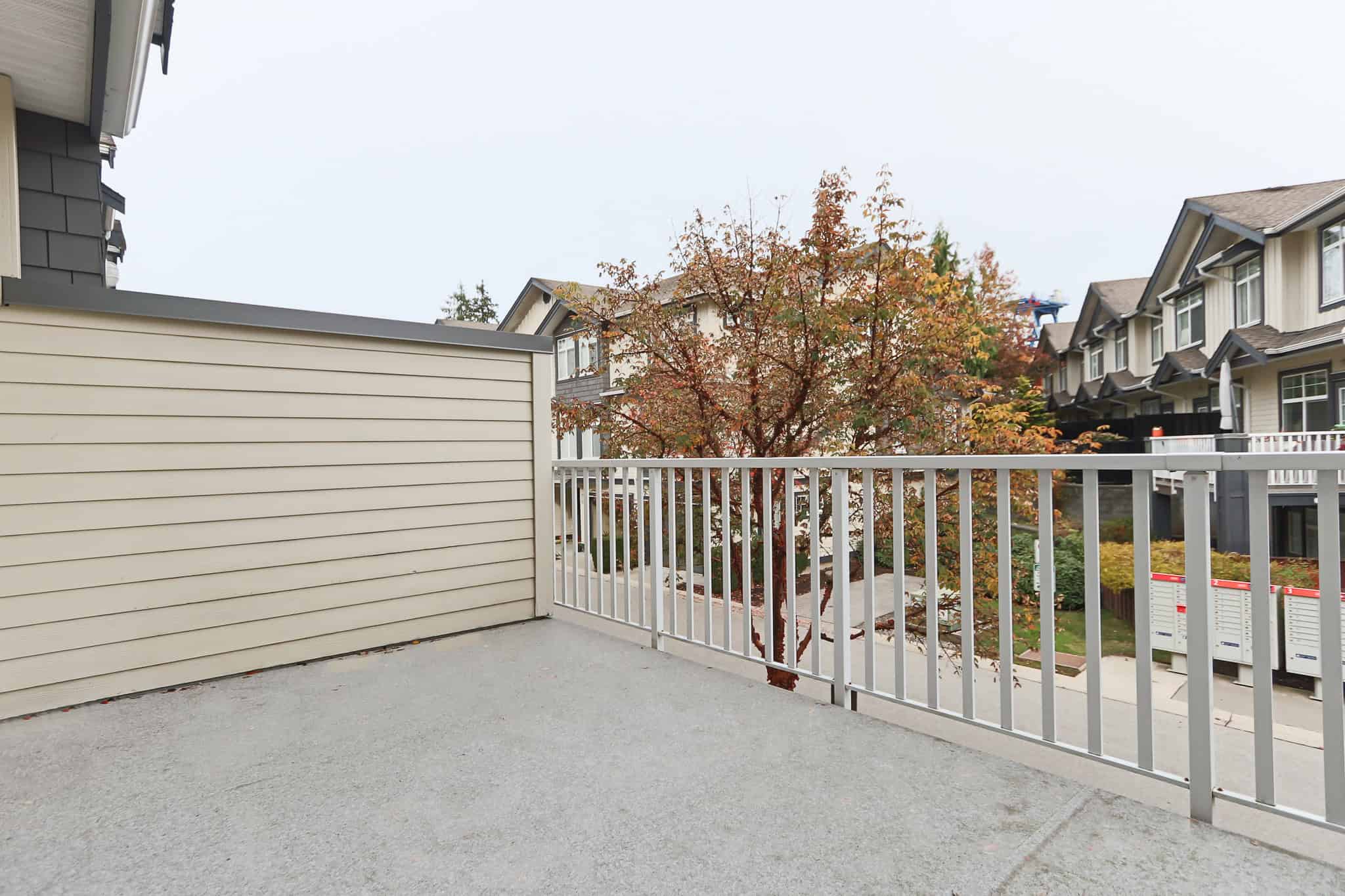 Bright balcony with beige siding, white railing, overlooking a tree with fall foliage in a modern Vancouver-area residential community.