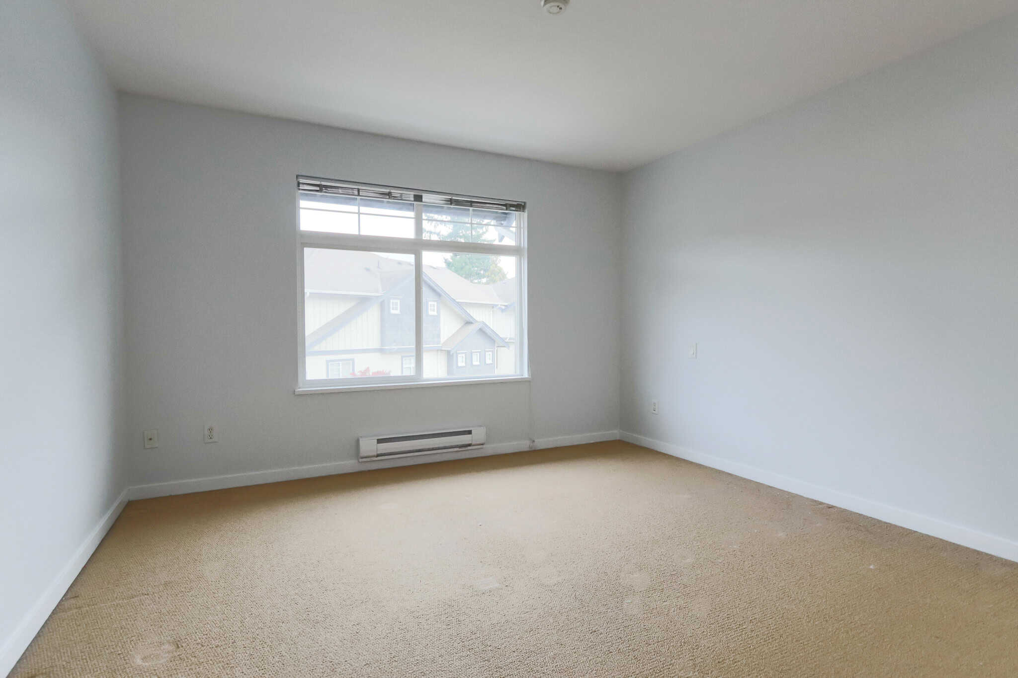 Bright spacious empty bedroom with large window in a modern home, featuring neutral wall color and beige carpet flooring, ideal for new homeowners or renters in Vancouver.