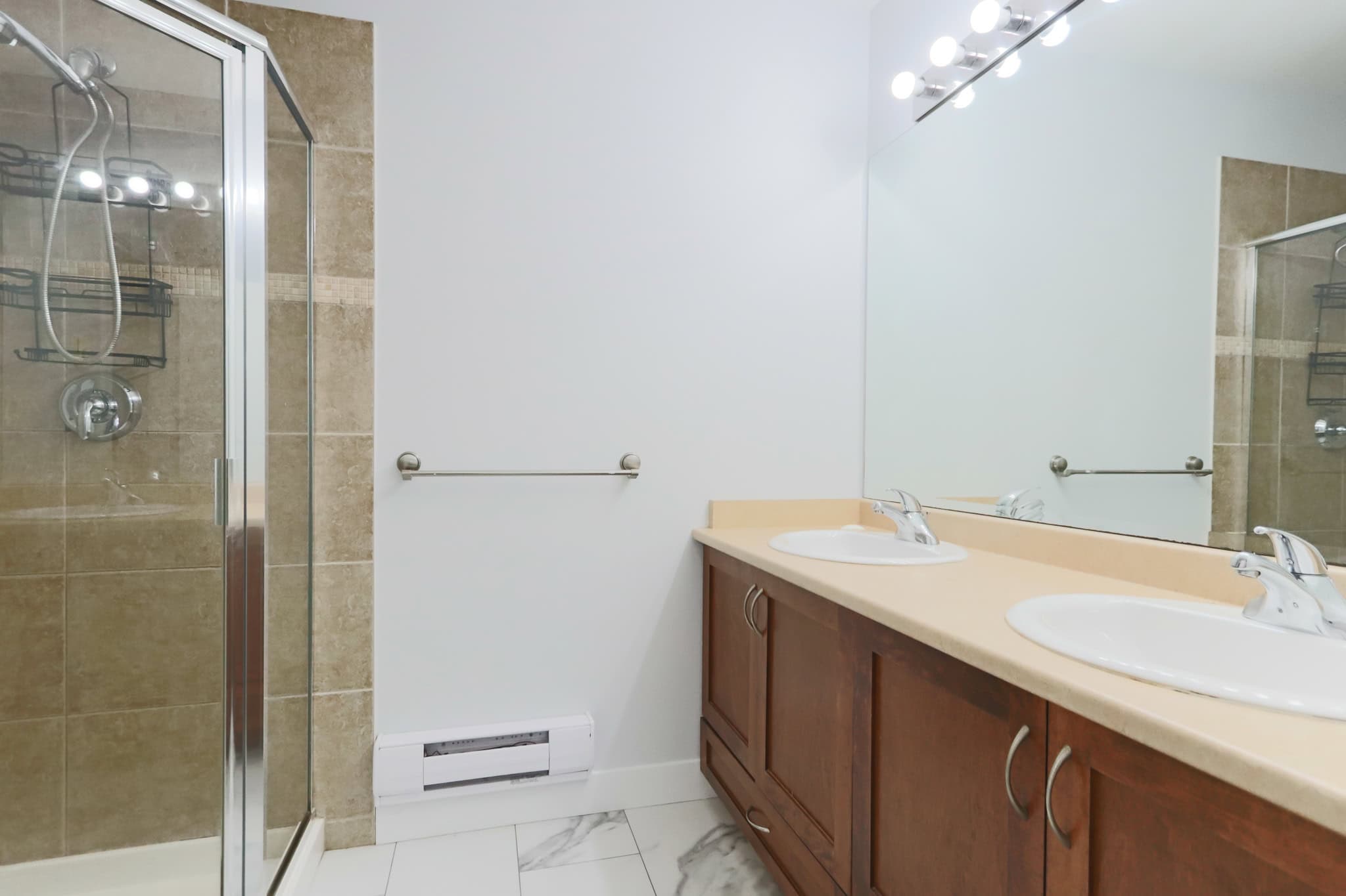 Spacious bathroom with double sinks and a walk-in shower featuring beige tile accents, modern fixtures, and ample storage, ideal for comfortable living in Victoria, BC.