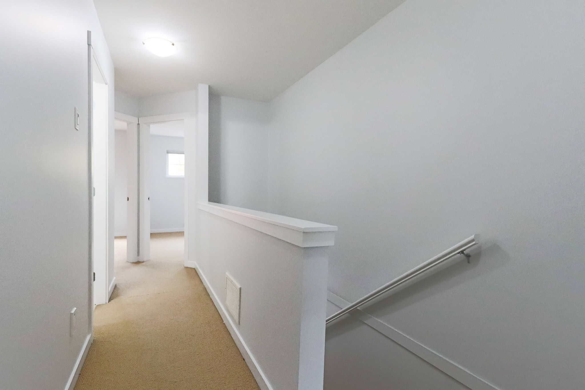 Bright, modern hallway in a residential home with white walls and beige carpet, showcasing clean interior design and natural light.