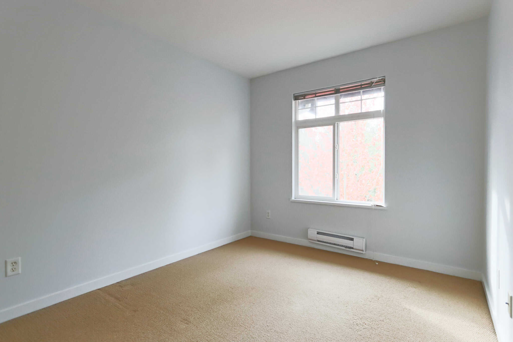 Bright, empty bedroom with natural light, white walls, and beige carpet, ideal for Vancouver Island real estate buyers seeking a cozy home in a peaceful neighbourhood.