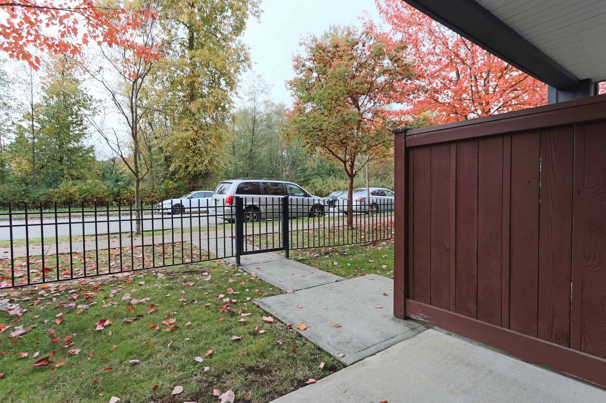 Modern residential front porch with black metal fence, green lawn, and vibrant autumn trees in the background, showcasing a cozy and inviting outdoor space for homes listed by Orca Realty Inc.