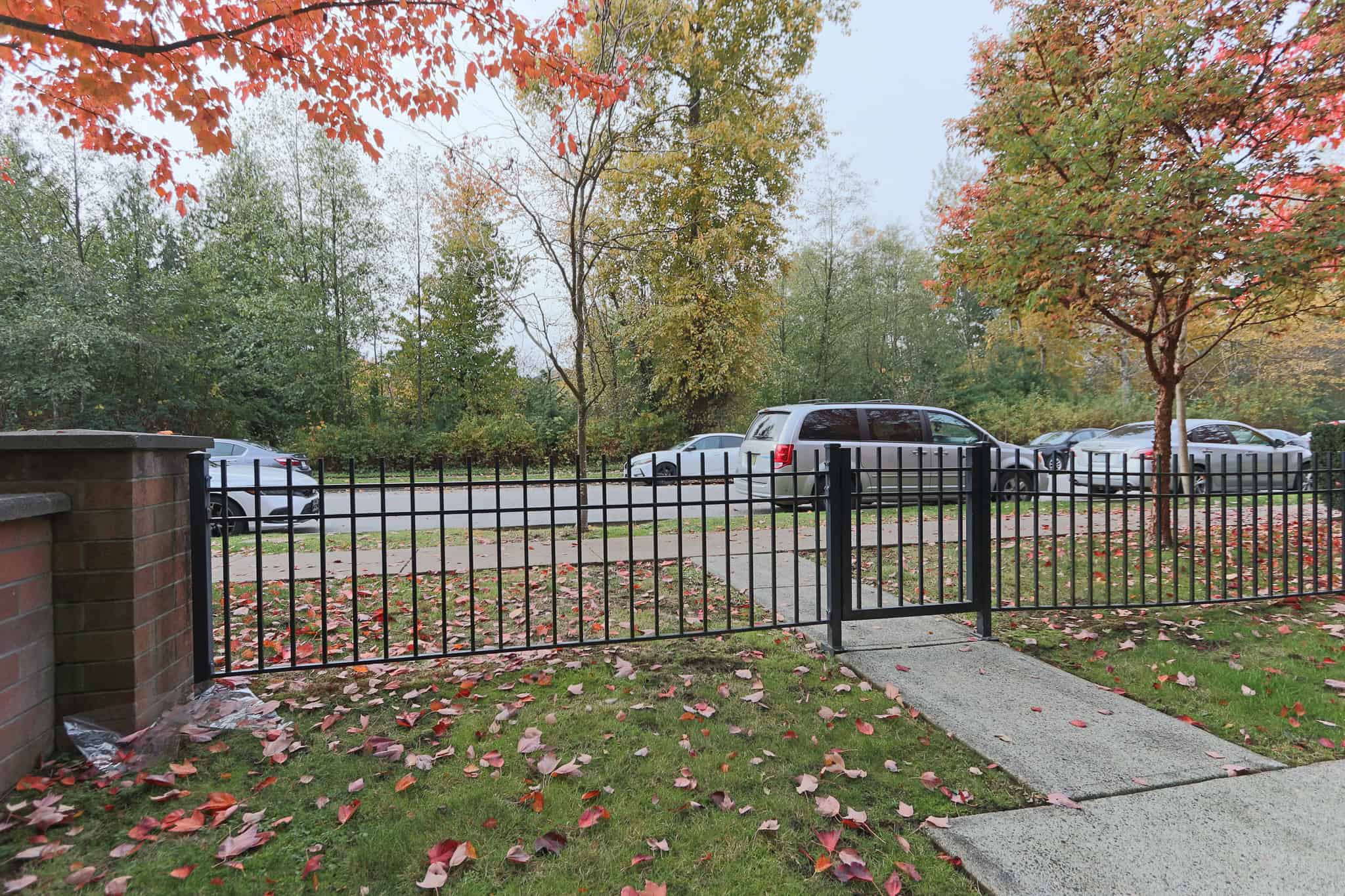Bright autumn scene at Orca Realty Inc. property with colorful fall foliage, parked cars, and a black metal fence along a sidewalk in a peaceful residential area in Canada.